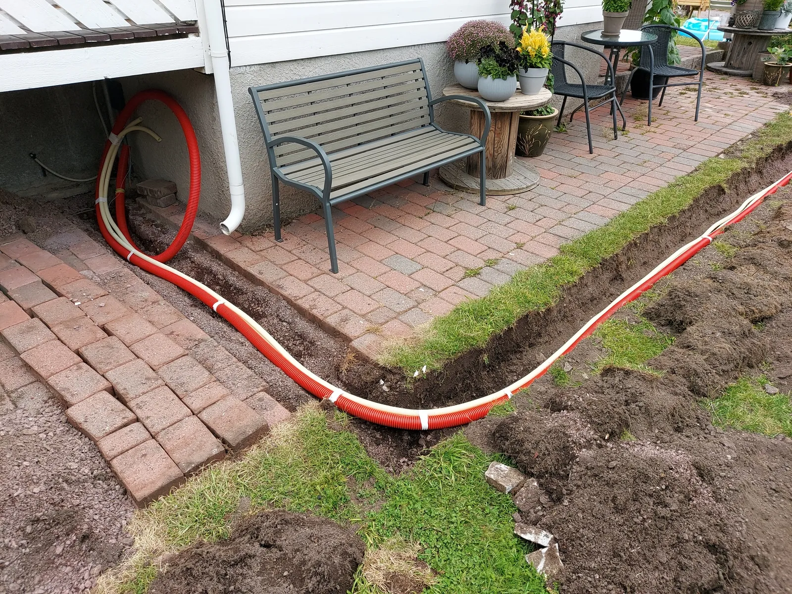 Shallow trench dug along a brick patio with red electrical conduit set in it